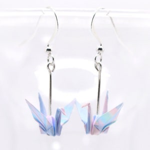 A pair of dangle earrings with origami cranes in a gradient pattern of pastel blues, pinks and purples. This photo shows a version of them that comes in a silver plated finish for the earring hooks.