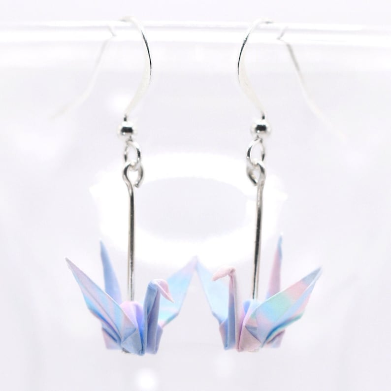 A pair of dangle earrings with origami cranes in a gradient pattern of pastel blues, pinks and purples. This photo shows a version of them that comes in a silver plated finish for the earring hooks.