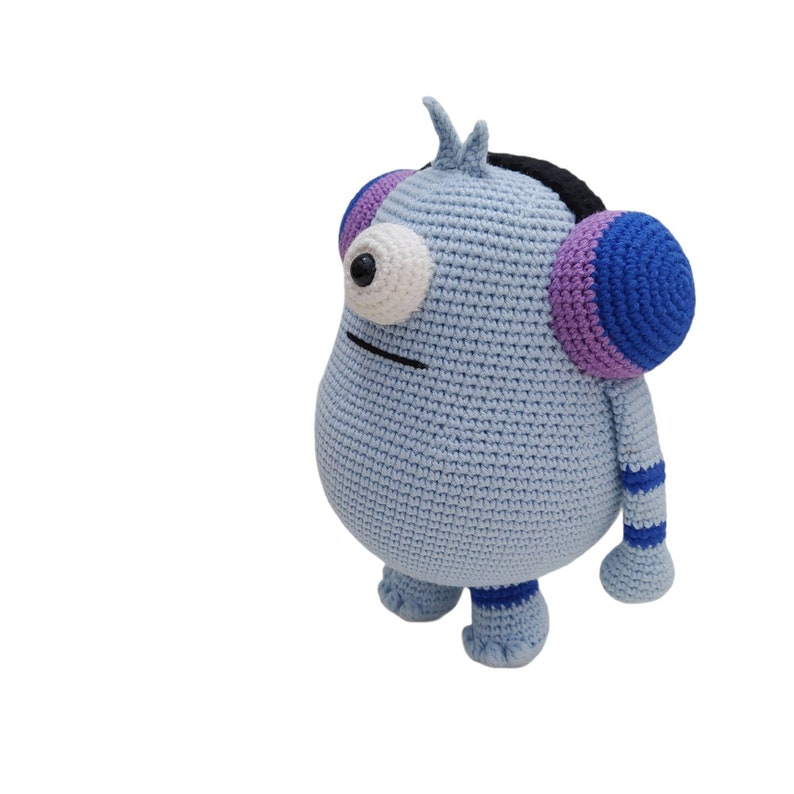 May include: A light blue crocheted monster toy with one large eye, a black headband, and purple and blue striped earmuffs.