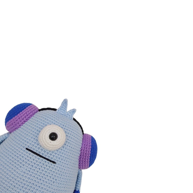 May include: A blue crocheted plush toy with a single eye and a purple and blue headband. The toy has a simple, stitched-on mouth.