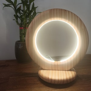 May include: A wooden vanity mirror with a circular light around the mirror. The mirror is on a wooden base and is lit up.