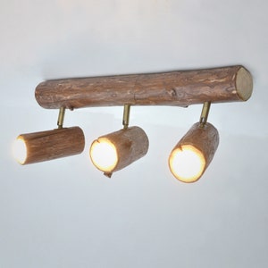 May include: A rustic ceiling light fixture made from a natural wood branch with three spotlights. The light fixture has a warm, natural wood finish and is perfect for adding a touch of rustic charm to any room.