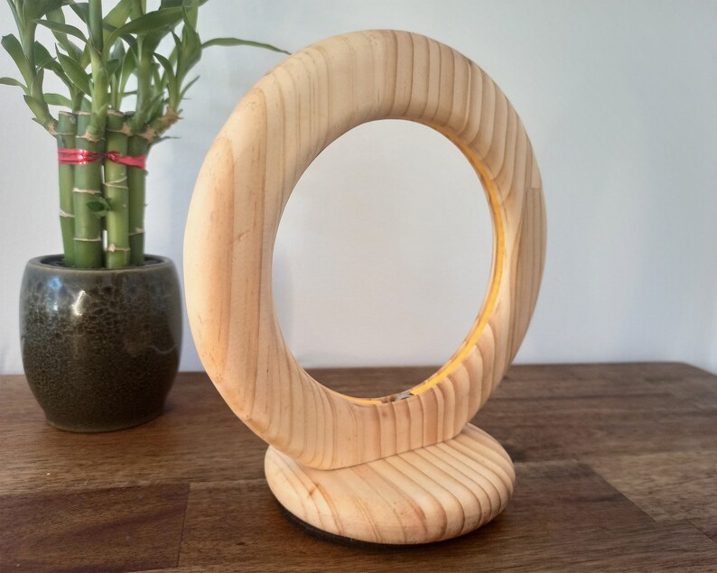 May include: A wooden ring stand with a natural wood finish. The stand is made of a single piece of wood and has a circular base. The ring is designed to hold a ring or other small object.