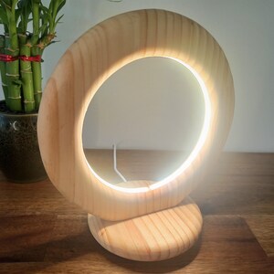 May include: A wooden table lamp with a circular light source. The lamp is made of natural wood and has a simple, modern design.