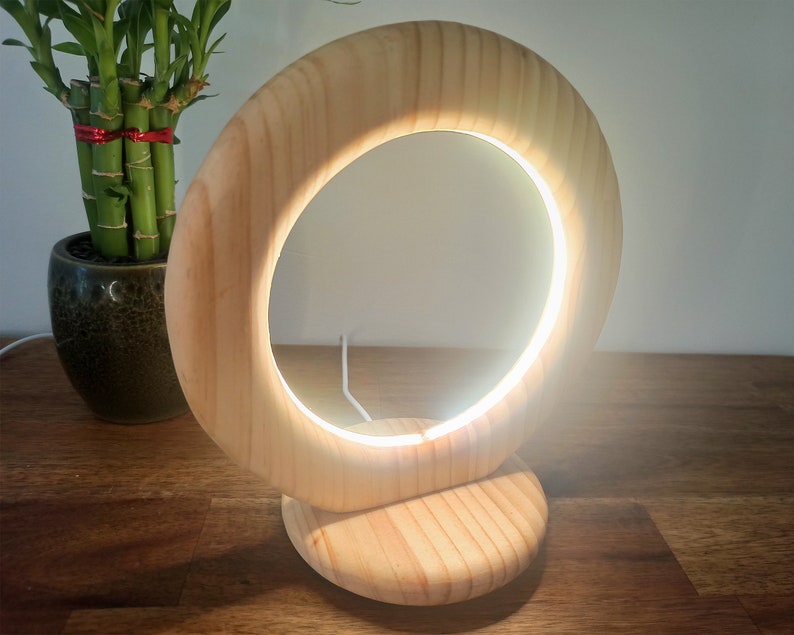 May include: A wooden table lamp with a circular light source. The lamp is made of natural wood and has a simple, modern design.