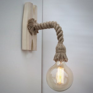 May include: A wall-mounted light fixture with a natural rope cord and a clear glass bulb. The fixture is attached to a wooden base.