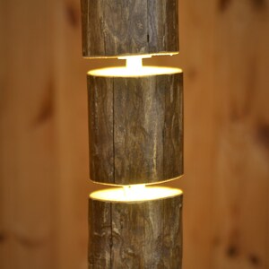 May include: A rustic, wooden pendant light fixture. The fixture is composed of three cylindrical wooden sections, stacked vertically with a warm, glowing light emanating from the spaces between them. The wood has a natural, textured appearance.
