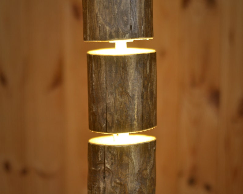 May include: A rustic, wooden pendant light fixture. The fixture is composed of three cylindrical wooden sections, stacked vertically with a warm, glowing light emanating from the spaces between them. The wood has a natural, textured appearance.