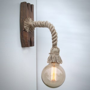 May include: A rustic wall sconce with a natural rope cord and a clear glass light bulb. The sconce is made of wood and has a natural finish.