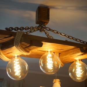 May include: A rustic wooden chandelier with three light bulbs. The chandelier is made of reclaimed wood and has a rope detail. The light bulbs are Edison bulbs and give off a warm glow.