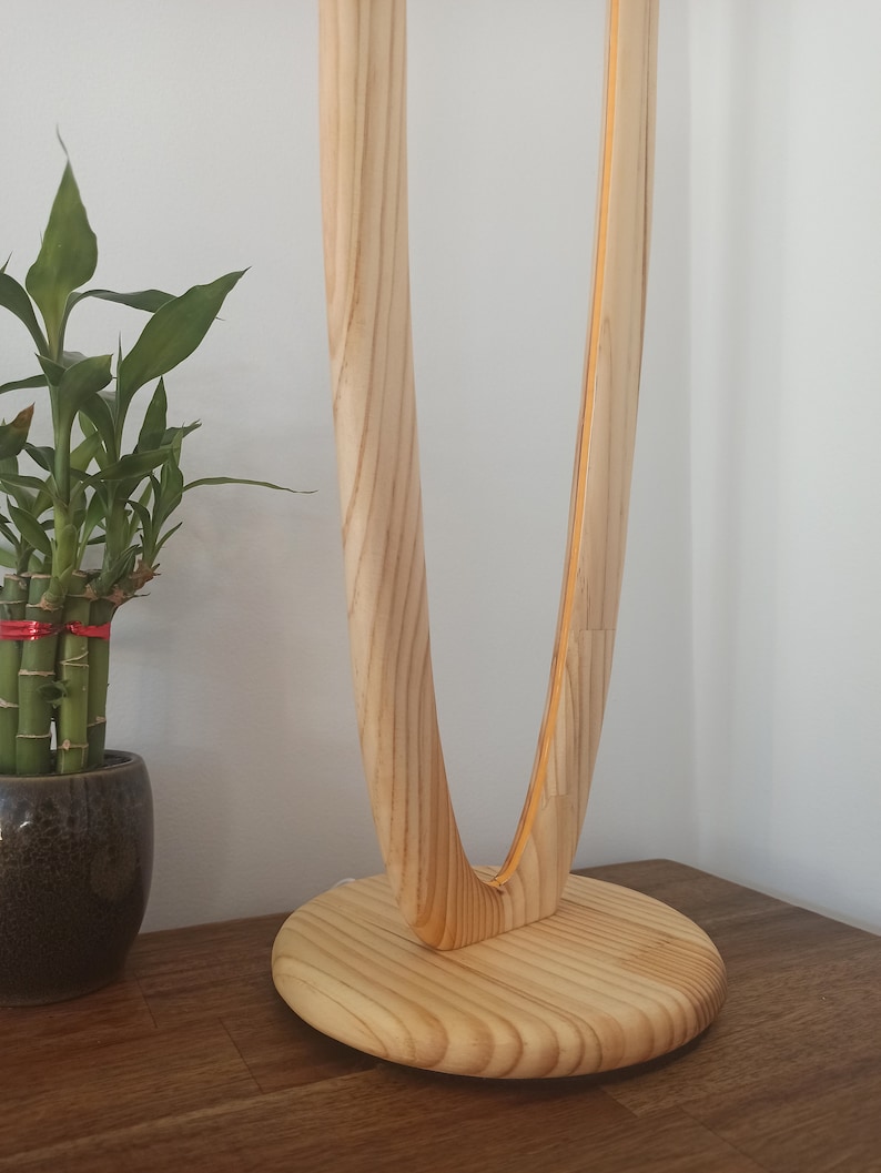 May include: A wooden table lamp with a unique curved design. The lamp base is made of natural wood and has a smooth, rounded finish.