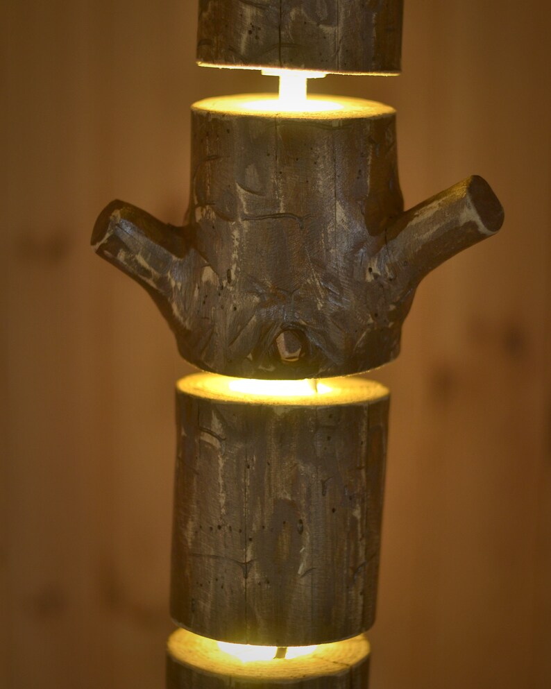 May include: A rustic, wooden lamp with a unique design. The lamp is constructed from stacked, cylindrical wooden pieces, with a branch-like element. Each section emits a warm, inviting light, creating a cozy ambiance. The lamp's natural wood tones and texture add a touch of nature to any space.