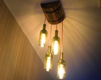 May include: A ceiling light fixture made from wine bottles with warm white light bulbs. The bottles are suspended from a wooden barrel-shaped base with red cords.