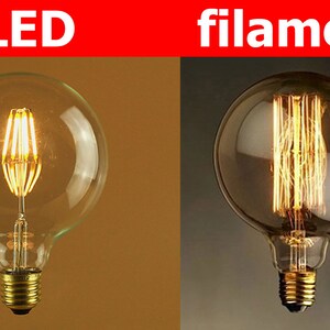 Puede incluir: Dos bombillas, una con una bombilla de vidrio transparente y un filamento LED, y la otra con una bombilla de vidrio esmerilado y un filamento tradicional. El texto "LED" est&aacute; sobre la primera bombilla y "filament" sobre la segunda.