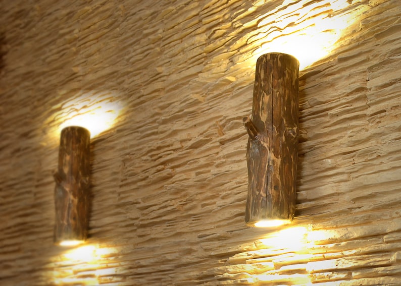 May include: Two rustic wooden wall sconces with light bulbs illuminating the room. The sconces are made from natural tree branches and have a warm, inviting aesthetic.