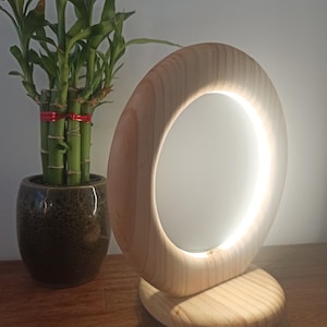May include: A wooden table lamp with a circular light source. The lamp is made of natural wood and has a warm, inviting glow.