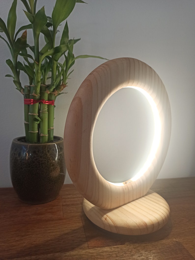 May include: A wooden table lamp with a circular light source. The lamp is made of natural wood and has a warm, inviting glow.