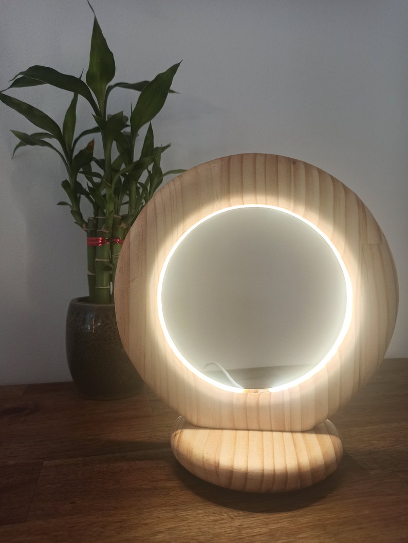 May include: A wooden vanity mirror with a circular light around the mirror. The mirror is on a wooden base and is lit up.