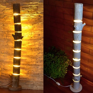 May include: A rustic floor lamp crafted from a section of a tree trunk. The lamp is segmented, with each section separated by a glowing light. The lamp has a natural wood finish and a round base.
