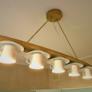 May include: A rustic wooden chandelier with five white porcelain teacups and saucers used as light fixtures. The chandelier is suspended from the ceiling with rope.