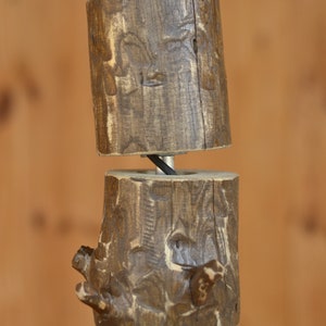 May include: A rustic wooden pendant light fixture. The fixture is made of several cylindrical wooden blocks, each with a unique, textured surface. The blocks are connected by a metal rod and a black wire. The wood has a warm, brown color.