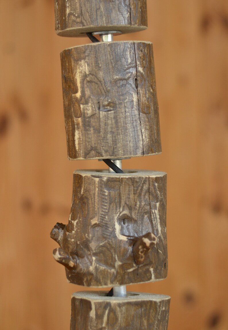 May include: A rustic wooden pendant light fixture. The fixture is made of several cylindrical wooden blocks, each with a unique, textured surface. The blocks are connected by a metal rod and a black wire. The wood has a warm, brown color.
