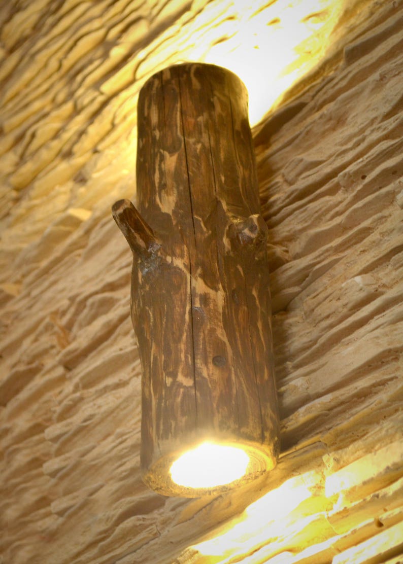 May include: A rustic wooden wall sconce with a light bulb inside. The sconce is shaped like a tree trunk with a branch extending out.