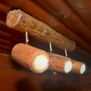 May include: A rustic wooden light fixture with three light bulbs. The fixture is made from a thick branch of wood with three smaller branches extending out to hold the light bulbs. The light bulbs are all turned on and emitting a warm white light.