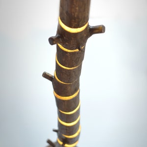 May include: A brown, tree-trunk-shaped lamp with a round base. The lamp has several small branches and emits a warm, yellow light from the cut-out sections. The lamp is made of wood and has a natural, rustic appearance.