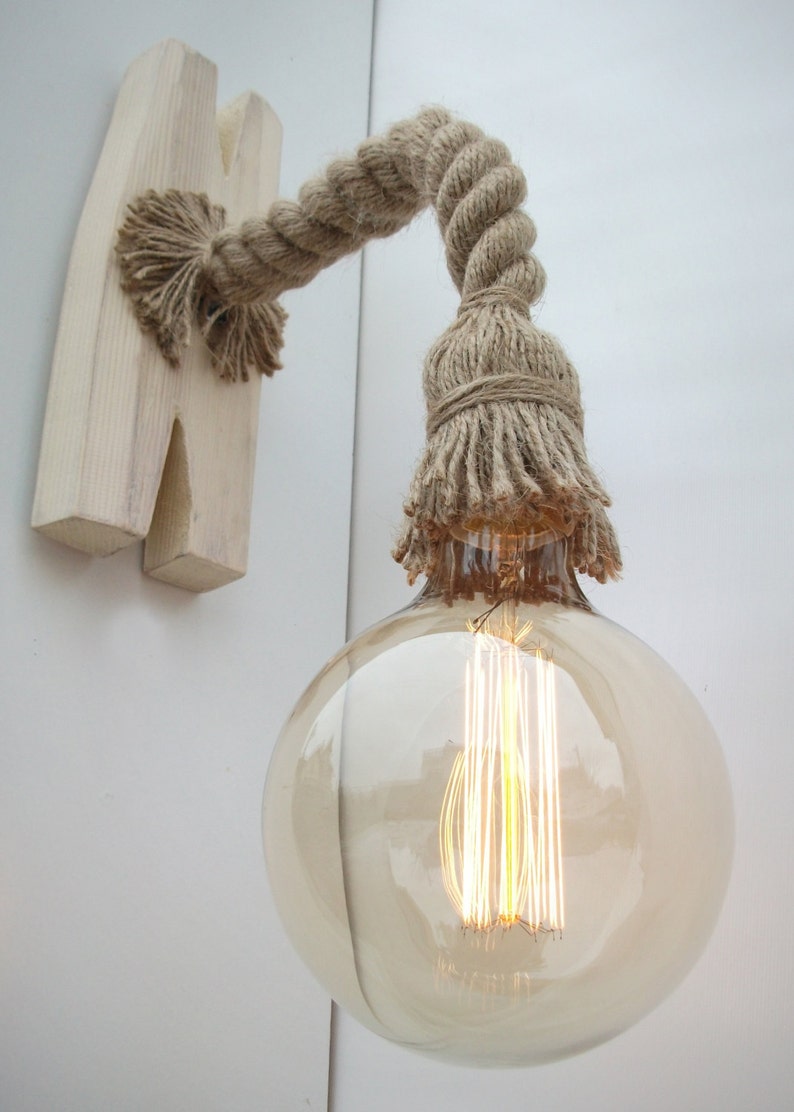 Puede incluir: Una l&aacute;mpara de pared r&uacute;stica con una bombilla, hecha de una base de madera y un cord&oacute;n de cuerda grueso. El cord&oacute;n de cuerda est&aacute; atado en un borla en el extremo, y la bombilla es un globo de vidrio transparente con un filamento.