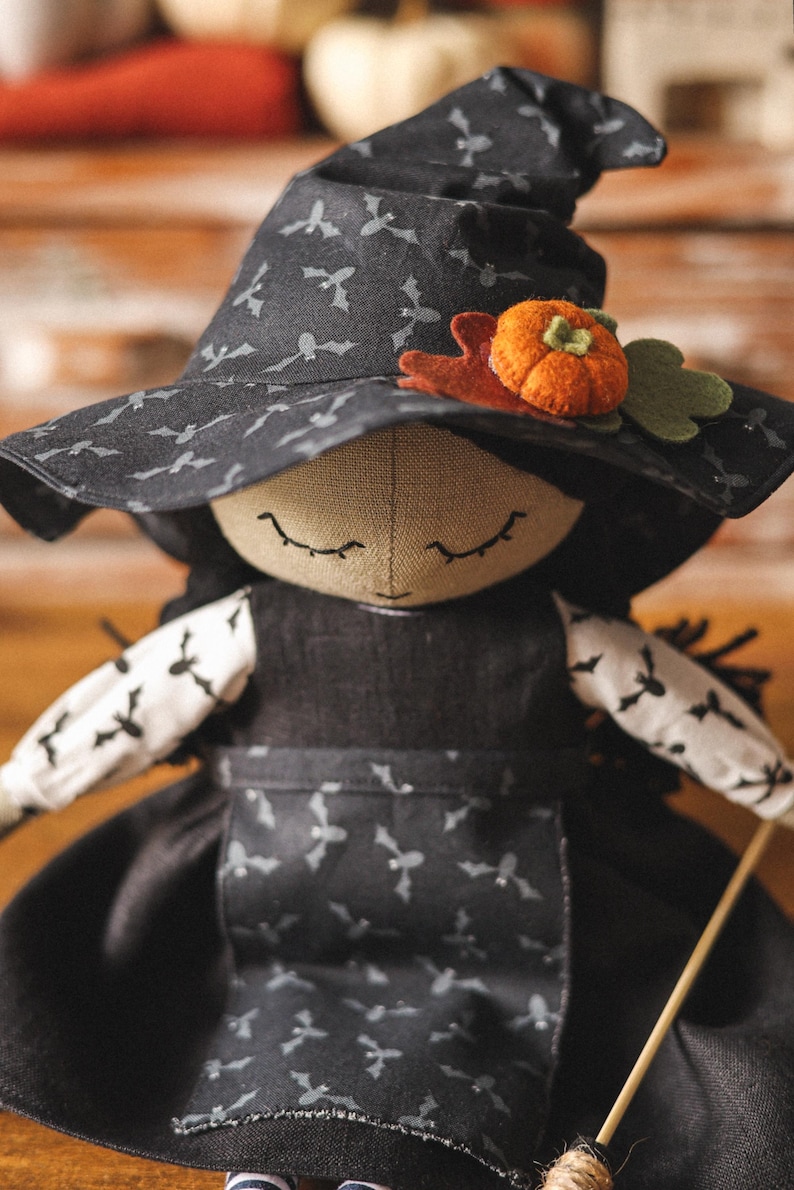 May include: A handmade witch doll with a black hat with bat silhouettes, a black dress with bat silhouettes, and a pumpkin and leaf embellishment on the hat.