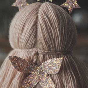 Op de afbeelding: Een handgemaakte pop met een lichtbruine garen hoofd en lichaam. De pop is versierd met glitterende stervormige haaraccessoires en een glitterende vlinder. De pop heeft een tule rok.