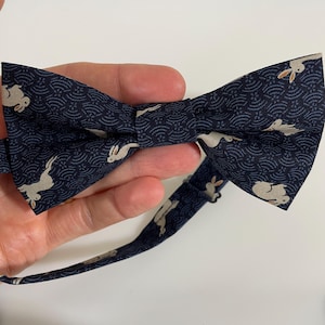 May include: A navy blue bow tie with a white rabbit pattern. The bow tie has a white strap.