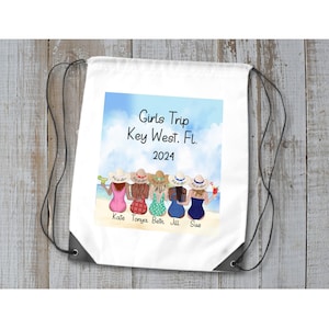 May include: White drawstring bag featuring a colorful illustration of six women on a beach, with the text "Girls Trip Key West, Fl. 2024." Each woman is wearing a different swimsuit and holding a drink. The names Kate, Tonya, Beth, Jill, and Sue are below the women.