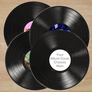 May include: Four black vinyl records are arranged on a light brown wooden surface. The records have visible grooves and colorful center labels. One label reads "Your Album Cover Choices Here".