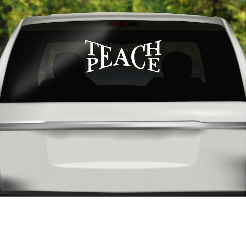 the rear window of a white car with the words "TEACH PEACE" written in large vinyl letters.