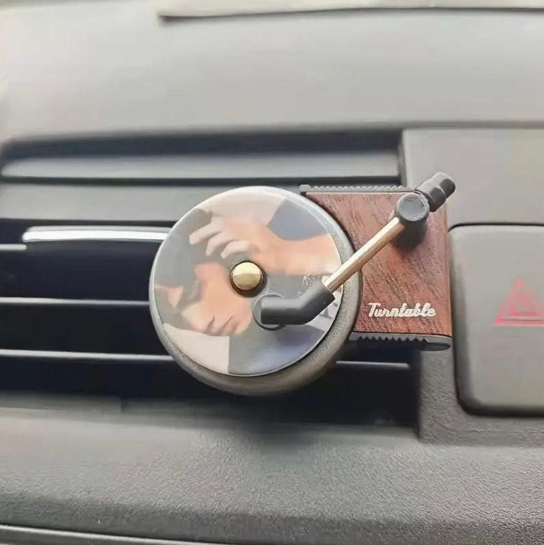 A car air freshener with a vinyl record player attached to it, which is placed on the dashboard of a vehicle.