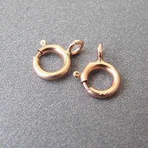 Könnte beinhalten: Zwei goldfarbene Metallverschlüsse zum Schmuckbasteln. Jeder Verschluss hat einen runden Ring mit einem federbelasteten Verschluss.