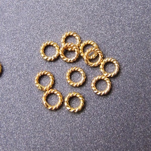 Könnte beinhalten: Eine Gruppe von 13 goldenen Sprungringen, einige sind verdreht, auf einer grauen Oberfläche.