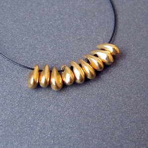 以下が含まれることがあります： 黒い紐に、涙滴型のビーズが連なった、金のネックレスです。