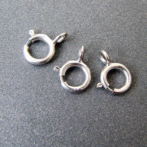 May include: Three silver-toned metal clasps for jewelry making. The clasps are round and have a spring-loaded closure.