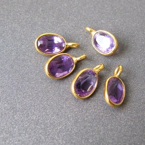 May include: Six gold-toned charms with oval-shaped amethyst stones. The charms have a loop at the top for attaching to a necklace or bracelet.