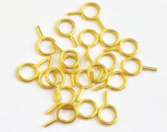 May include: A pile of gold-colored metal jump rings with a small loop on one side and a straight pin on the other side.