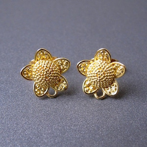 May include: A pair of gold-tone flower-shaped earrings. The earrings have a textured surface and a delicate design.