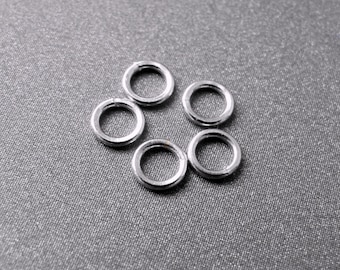 May include: Six silver jump rings arranged in a circle on a gray background.