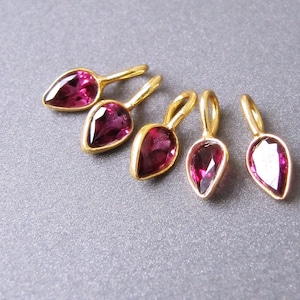 Op de afbeelding: Vijf gouden hangers in druppelvorm met roze edelstenen. De hangers zijn aan een gouden ketting bevestigd.