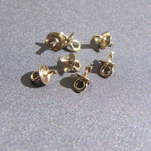 May include: Six gold-toned metal jewelry findings with a loop on one end and a flat disc on the other. These findings are used for attaching jewelry components.