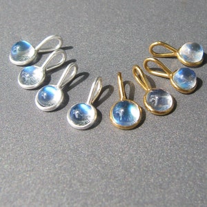 Könnte beinhalten: Sechs silberne und goldene Anhänger mit schillernden blauen Mondstein-Steinen. Die Anhänger sind alle oval geformt und haben eine Öse oben zum Anbringen an einer Kette.