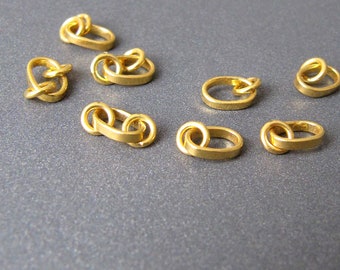 May include: A collection of eight gold-toned metal jump rings, some with a double loop design, for jewelry making.