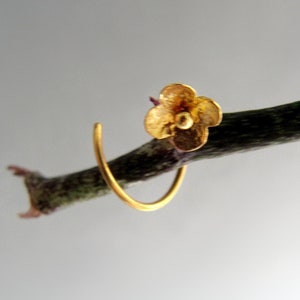 K&ouml;nnte beinhalten: Ein goldener Ohrring in Bl&uuml;tenform mit einem einfachen Kreisdesign. Der Ohrring h&auml;ngt an einem Zweig.